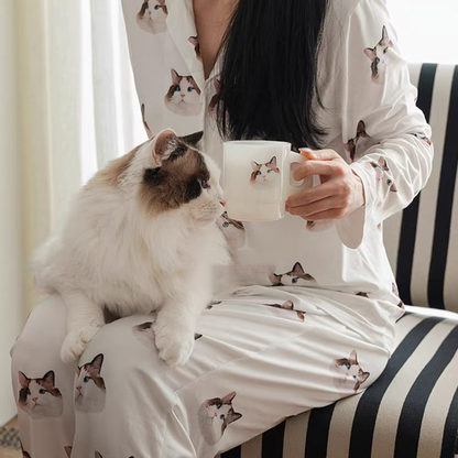 A person sitting with a white cat on their lap, wearing custom unisex milk silk pajamas set with pet faces printed on it.