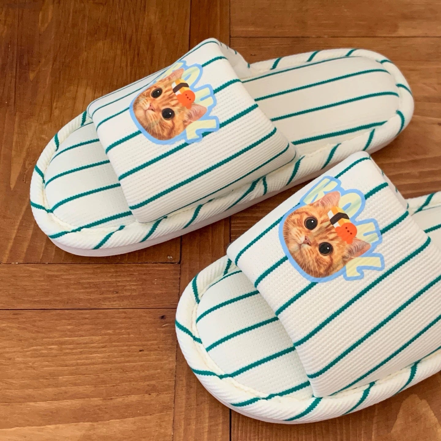 Pair of striped slippers with cat face designs on a wooden floor