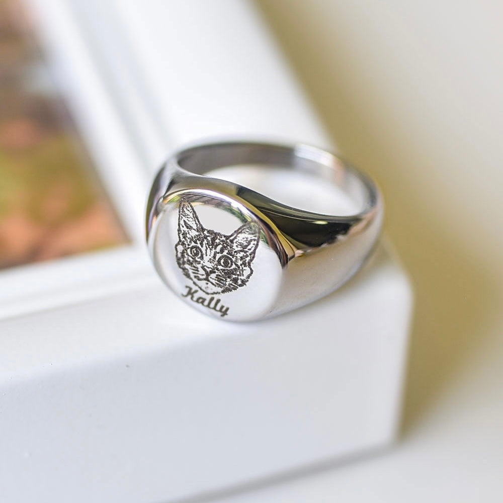 A silver ring with an engraved image of a pet and the name 'Rex' on a surface.