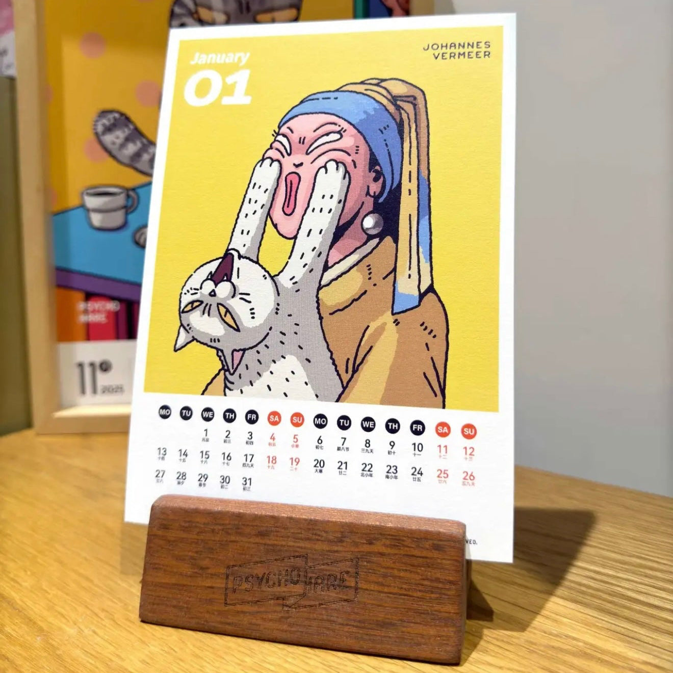 A whimsical illustrated pet calendar for April, featuring a colorful cartoon of a person with a cat, placed on a wooden stand.