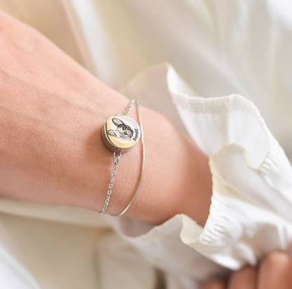 A close-up image of a personalized pet bracelet with a locket charm, featuring an engraved pet portrait, worn on a person's wrist.